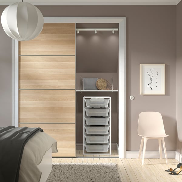 Modern closet with wooden doors and metal baskets. A white chair rests beside it. A bed and a rug are partially visible.