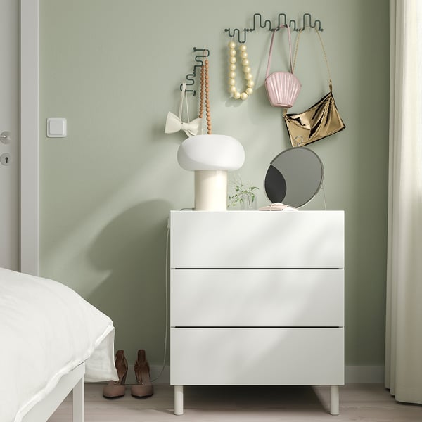 White hook on green wall holding bags & beads, minimalist room with dresser & bed.
