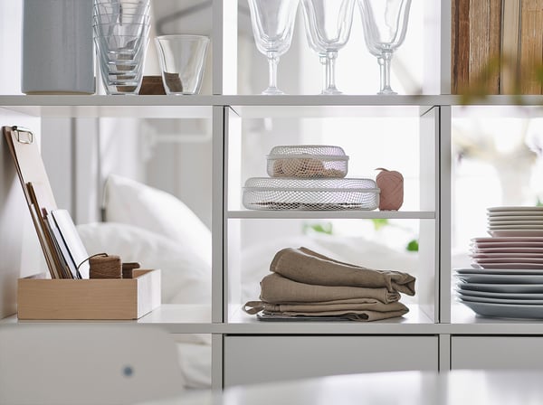 White KALLAX shelves display glassware, folded linens, and dishes neatly.
