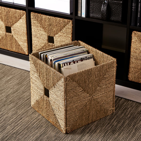 Woven seagrass basket on floor, filled with magazines, ideal for kallax shelves.