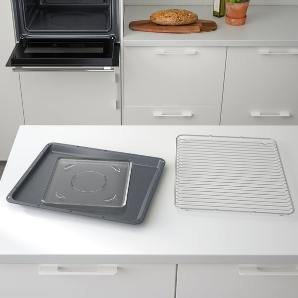 Modern kitchen with built-in oven and trays. Two trays sit on a white countertop beside the oven. One is non-stick, the other a wire rack.