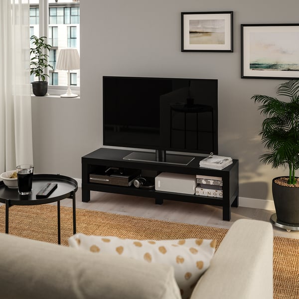 Modern living room with bLACK tv bench, flat-screen tv, cosy sofa, side table, and floor lamp with plant.