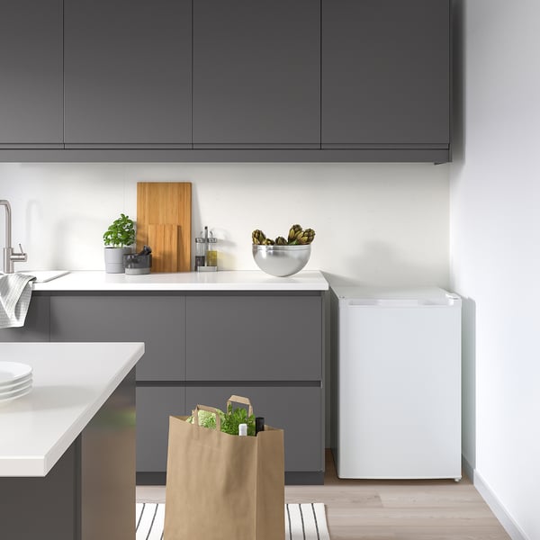 Compact grey kitchen with white fridge, plants, bowl, and cutting board on wooden floor.