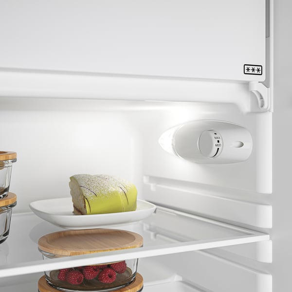An open refrigerator with a cake and raspberries inside. The control panel indicates its a freestanding model with an integrated led light.