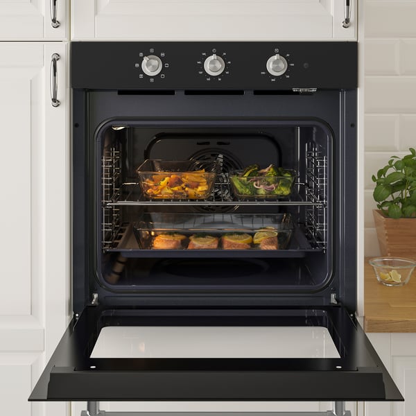 Black oven with fan-forced convection cooking multiple dishes. Glass door open displaying trays of food inside.