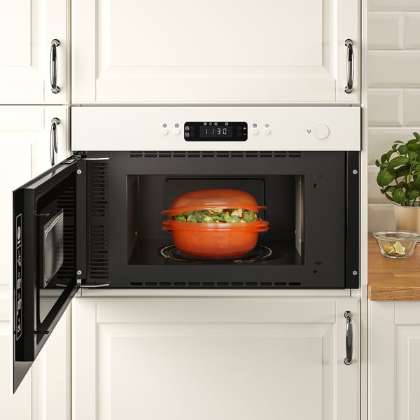 Open microwave heating orange dish with vegetables. Modern kitchen setting.