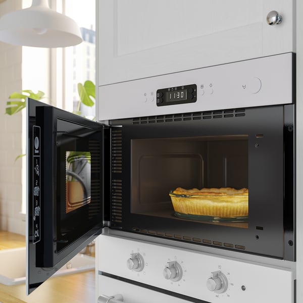 Open white microwave oven with a pie inside, digital display above, set in a white kitchen.