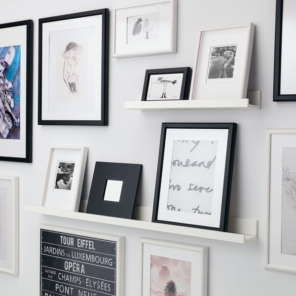A wall-mounted shelf displays various framed photos in a gallery style. The shelfs groove securely holds smaller frames upright.