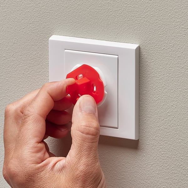 Hand inserts red key into white safety plug, blocking socket for child safety.