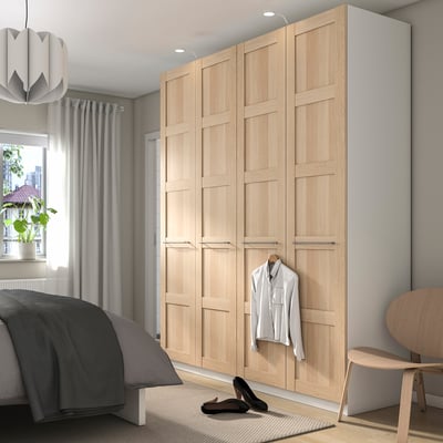 Wooden PAX wardrobe next to bed, plant by window.