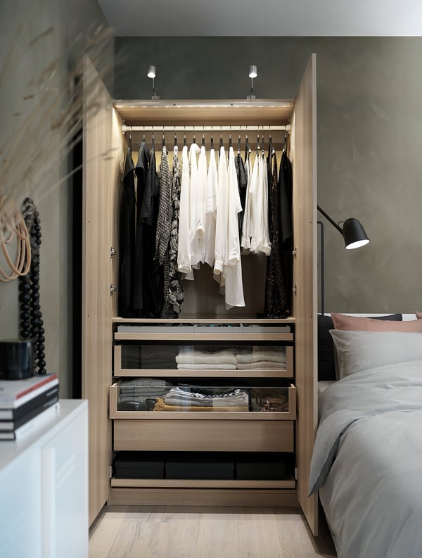 Open wooden closet, black and white clothes, shelves, drawers, soft lighting.