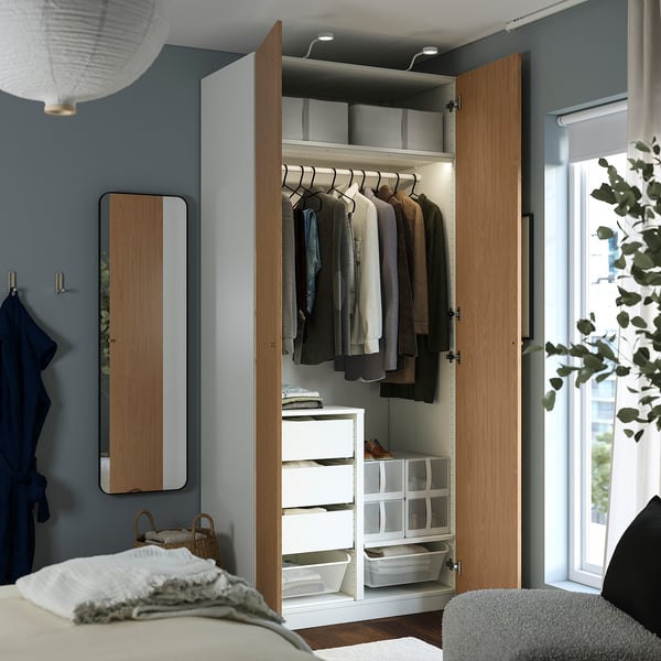 Open wood wardrobe with garments, shelves, and drawers. Light illuminates stored clothes and accessories.