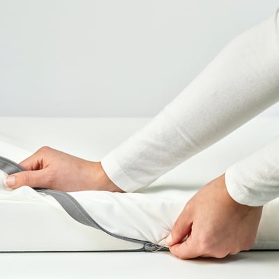 Person zips grey and white bed sheet, showcasing its reversible design and child-safe zip.