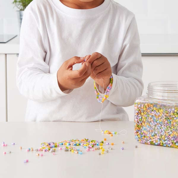 Child threading colourful beads onto string at table, creating art with PYSSLA beads.