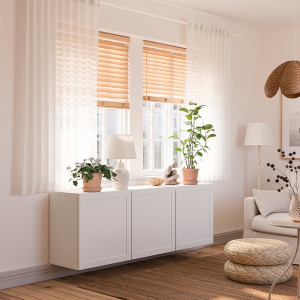 Bright living room with large window, sheer curtains, modern cabinet, plants, chair, and lamp.