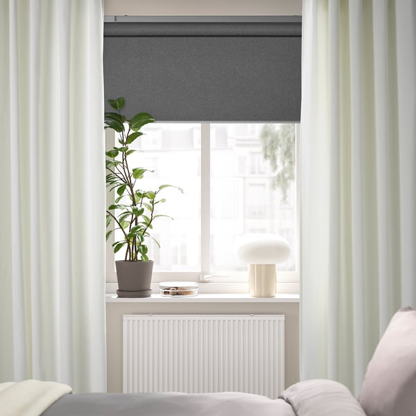 Minimalist window: roller blind, plant, lamp, radiator, partial bed, SANELA curtains.