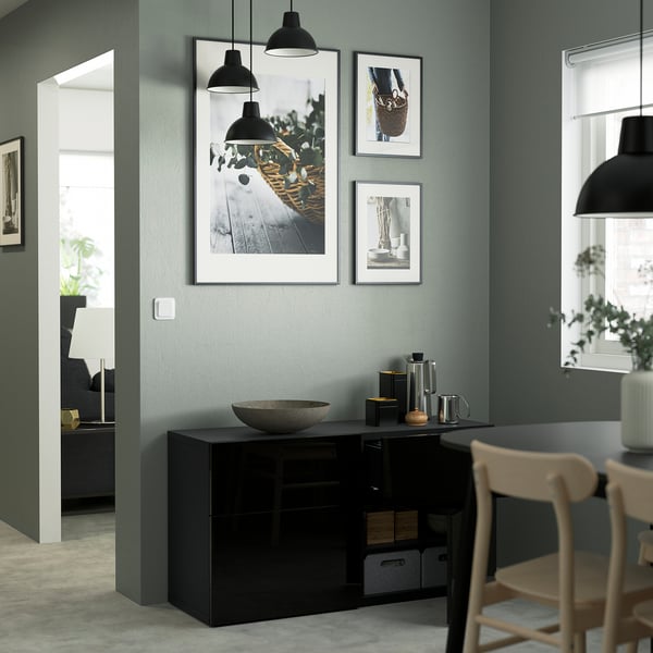 Modern dining area with black glossy storage unit featuring a door and drawers, under three framed art prints, lit by black hanging lamps.