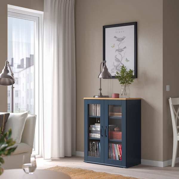 Dark blue SKRUVBY cabinet with glass doors, books, lamp, vase, chair & wine glass.