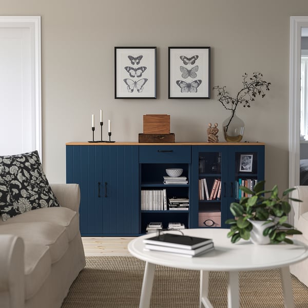 Modern living room: beige sofa, blue SKRUVBY sideboard, white coffee table, butterfly prints, candles, books, plant.