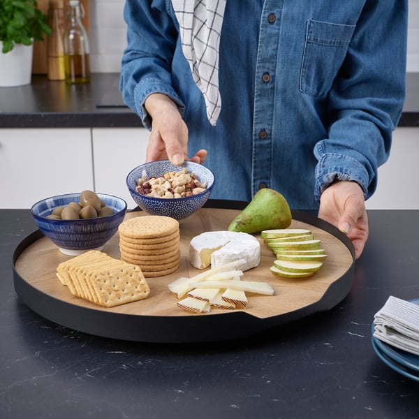 Person holding cheese tray with snacks on black counter.