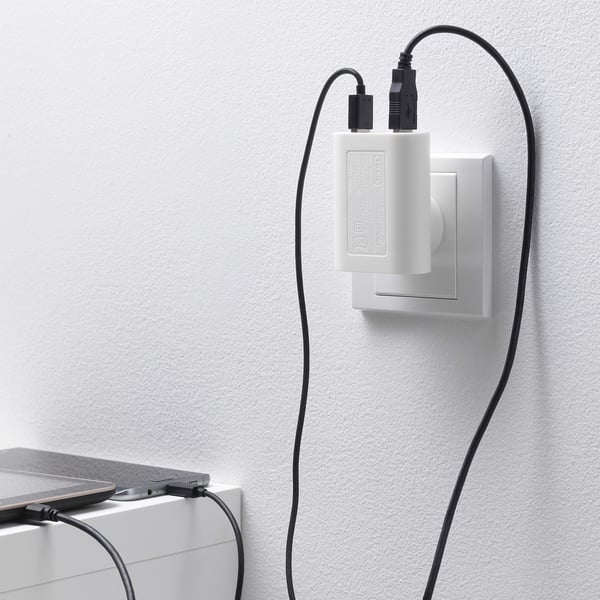 A white wall-mounted charger with 3 usb ports, charging a smartphone, showing its functional aspect of charging multiple devices simultaneously.