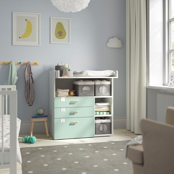 Baby room with blue SMÅSTAD changing table & dresser near window. Room crib, light blue walls, cloud pendant light, & baby supplies.