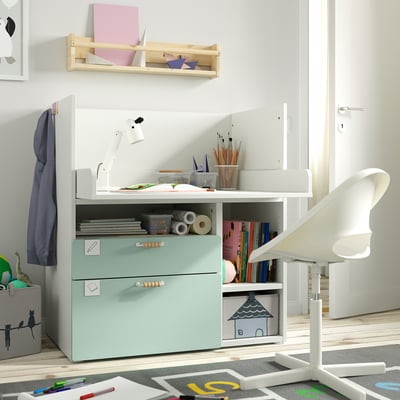 Kids study spot with mint desk, books, art supplies. Blue jacket, white chair, wooden shelf with books.