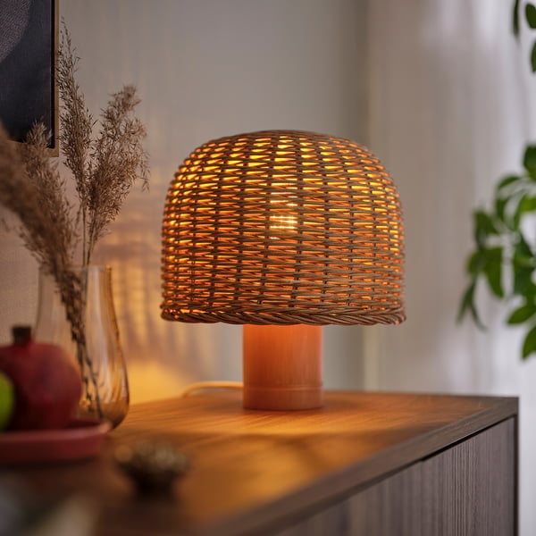 Woven led table lamp emits warm, soft glow on wooden shelf with decor.