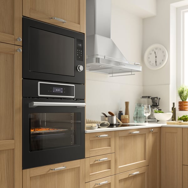 Modern kitchen with black IKEA STENABY oven, microwave, & digital display in wooden cabinets. Well-lit with white countertop & clock.
