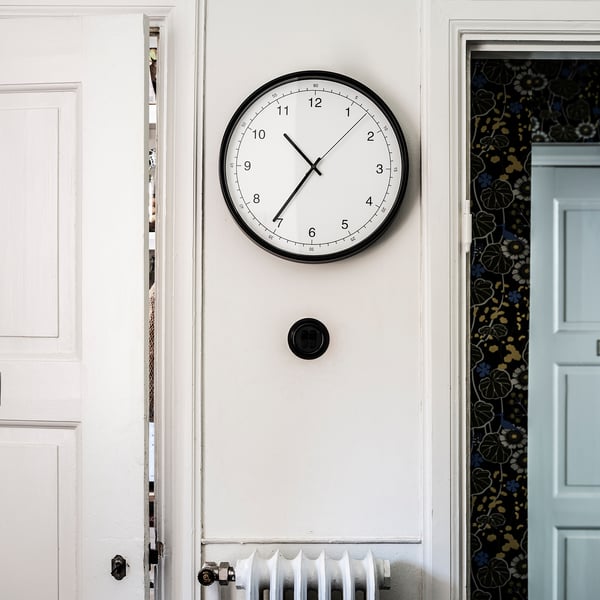 A round, black-sleeved wall clock with a white face and black hands, showing 10:10, mounted between two white doors with floral patterns.