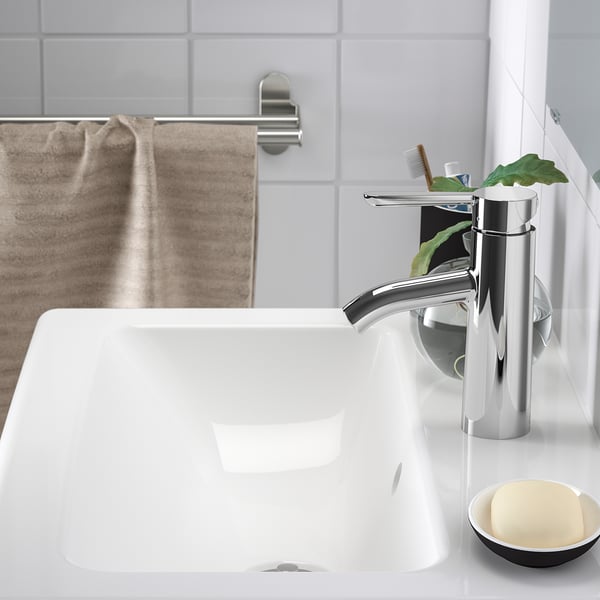 Modern bathroom sink with chrome tap and soap dish, set against white tiled wall and beige towel.