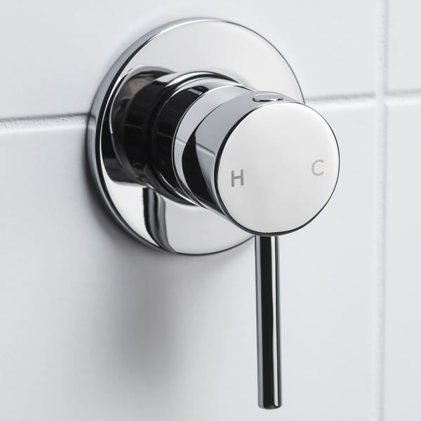 Chrome shower mixer with h/c knobs, close-up on tiled wall, sleek design.