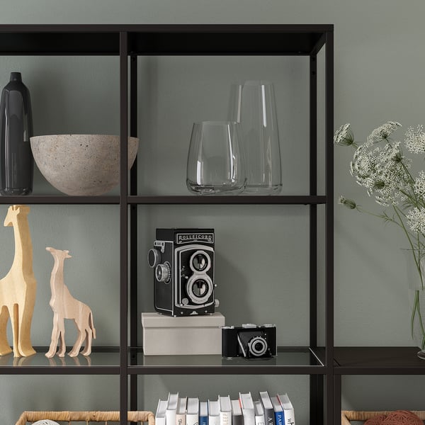 Shelf unit with glass shelves displaying decorative items. Adjustable feet for stability.