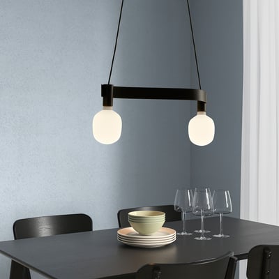 Modern ACKJA lamp with frosted globes above black dining table, focusing on stacks of plates, bowls, and wine glasses.