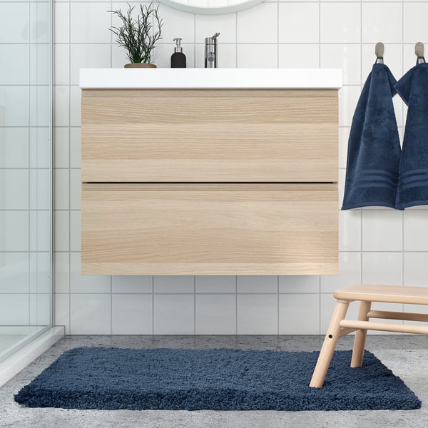 Modern bathroom with wooden vanity, blue rug, and bench. Dark blue ALMTJÄRN mat, soft and absorbent, fits well under the bench.