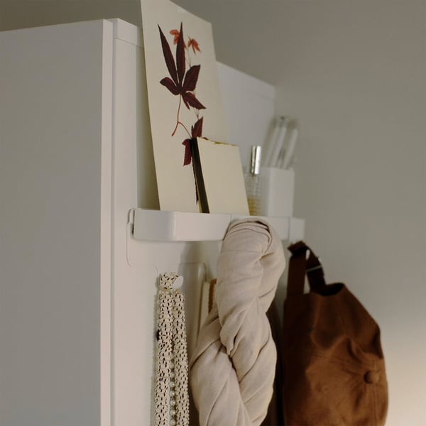 White wall rack with hanging items: cloth, necklace, and artwork.