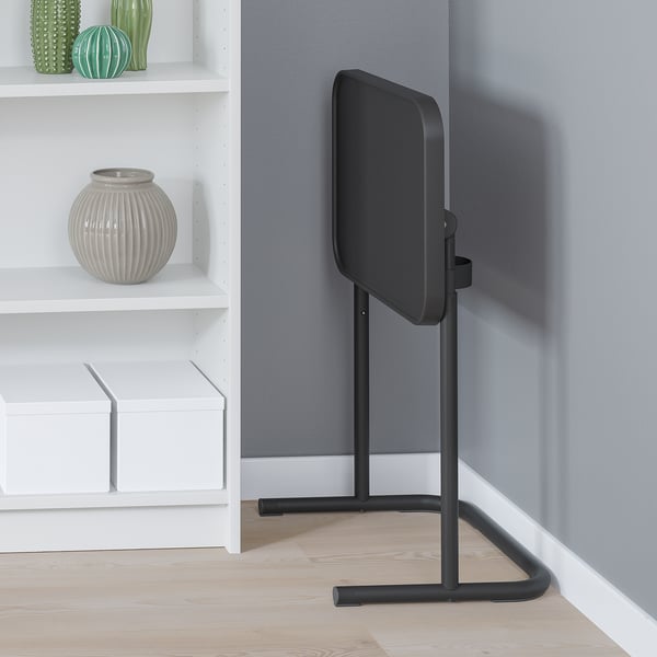 Black laptop stand rests against grey wall, next to white shelf with vases.