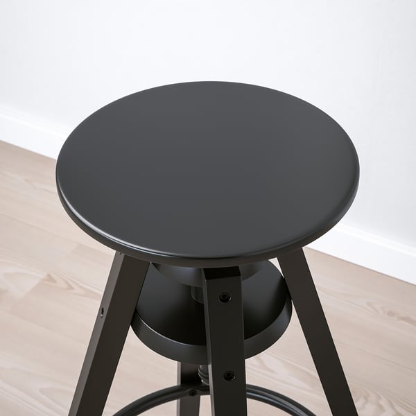 Black round stool with adjustable height on wooden floor. Modern design with sturdy metal legs and smooth seat.