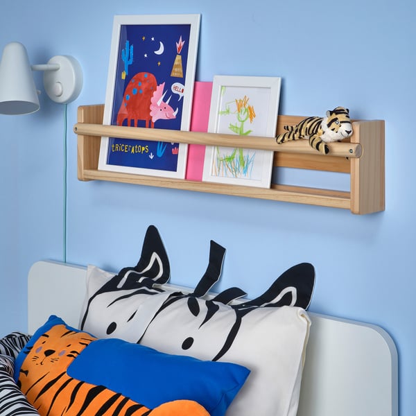Kids room with blue wall, art shelf, DJUNGELSKOG toy, zebra pillow bed, lamp, drawing.