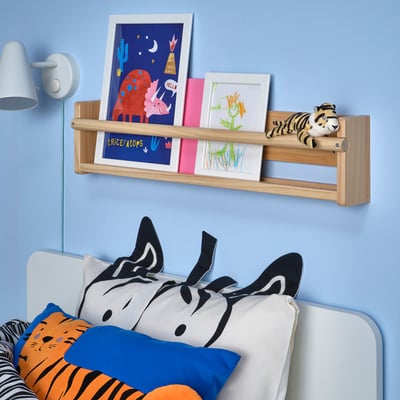 Kids room with blue wall, art shelf, DJUNGELSKOG toy, zebra pillow bed, lamp, drawing.