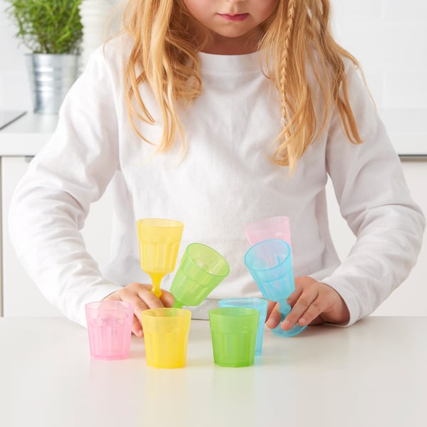 A child playing with colourful plastic cups and goblets, arranging them on a table.