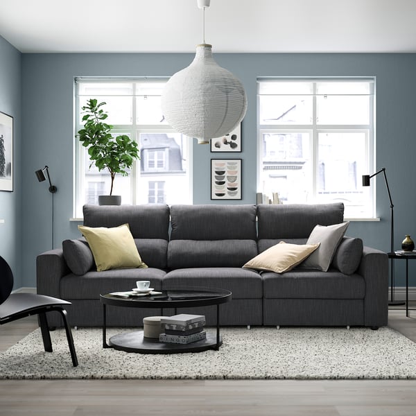 Modern living room with grey sofa, rug, and large windows. Spacious sofa with cushions and sleek coffee table.