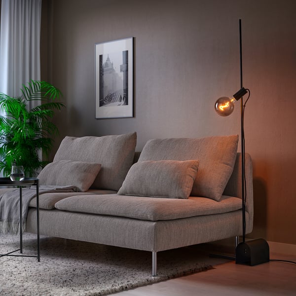 Modern living room with HÅRSLINGA lamp lighting grey sofa, plant, and picture.