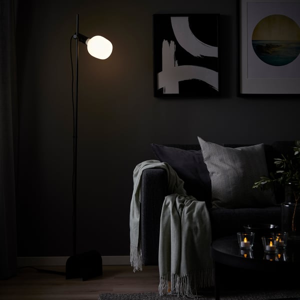 Modern living room with HÅRSLINGA floor lamp, couch, blankets, pillows, art, and candles.