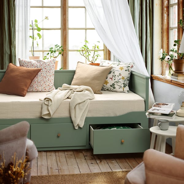 HEMNES day-bed in grey-green, sofa/bed with storage, pillows, blanket, plant, cup.