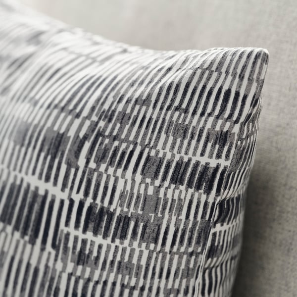 Close-up of a soft, patterned throw pillow on a bed. Grey and white geometric design on textured fabric.