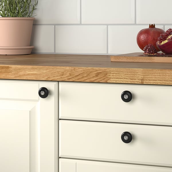 Wooden countertop with white cabinet, matte black knobs, pomegranate, and plant.