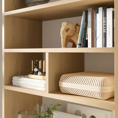 Wooden bookshelf with LÅDMAKARE storage. Top: books, wooden elephant. Bottom: decor, books, woven box.