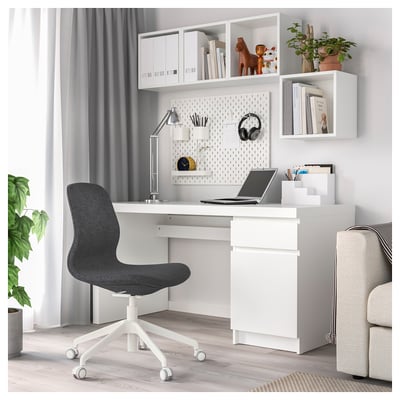 Modern home office setup: white desk, black chair, shelves with decor, laptop, lamp, pegboard.