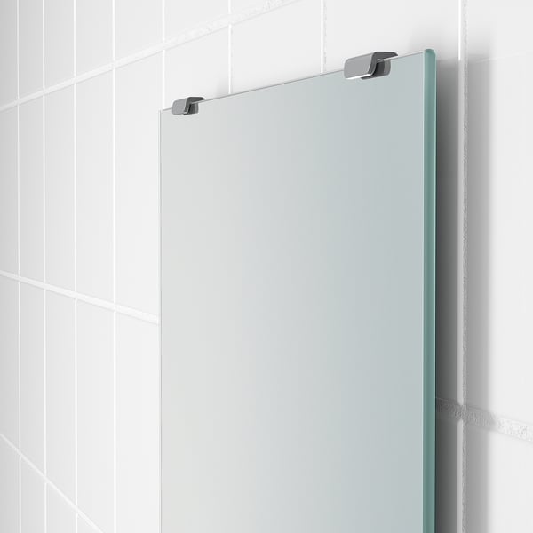 Modern mirror mounted in bathroom with chrome hinges, polished edge, reflecting bright light.